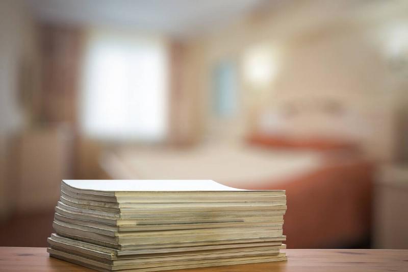 A stack of papers in focus in front of a bed. 