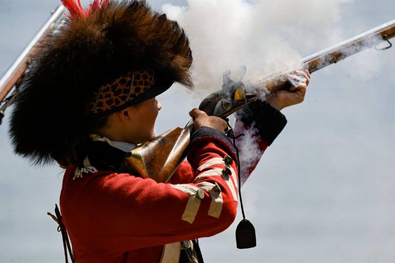 Re-enactor firing a rifle while dressed as a British soldier in the American Revolution