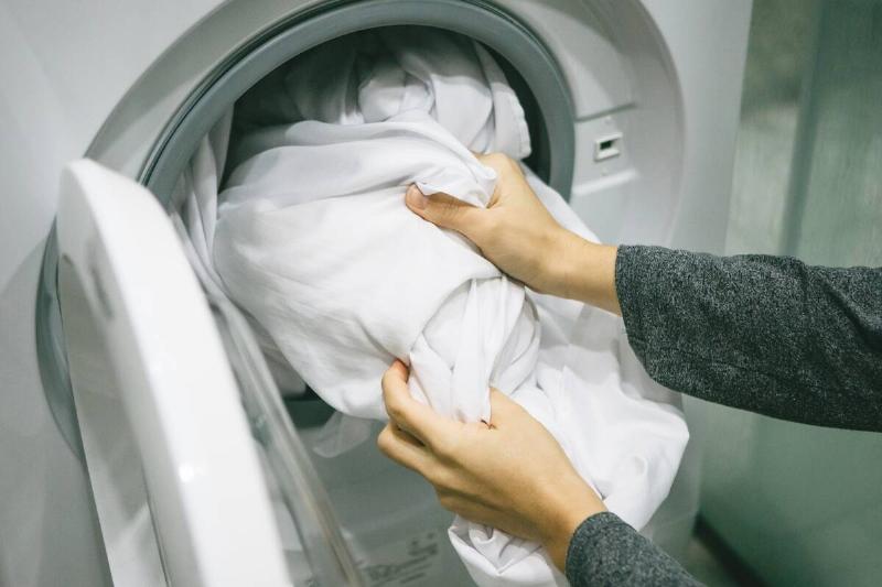 Person putting sheets in the washing machine. 