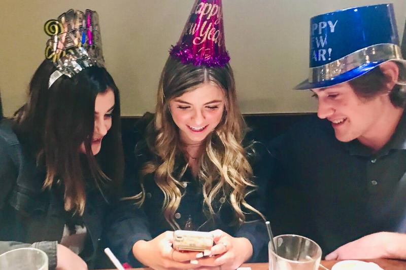 Three friends wearing NYE at a and looking at a phone. 