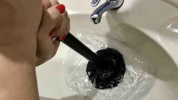 Hands using plunger to unclog sink. 