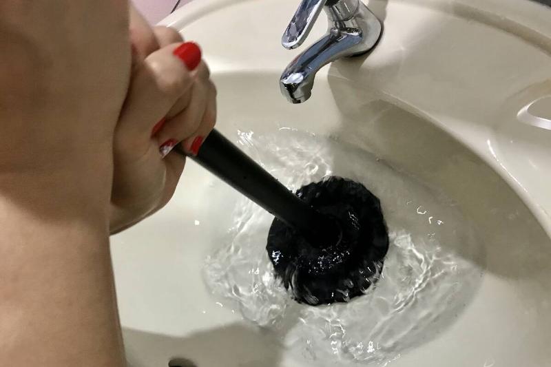 Hands using plunger to unclog sink. 