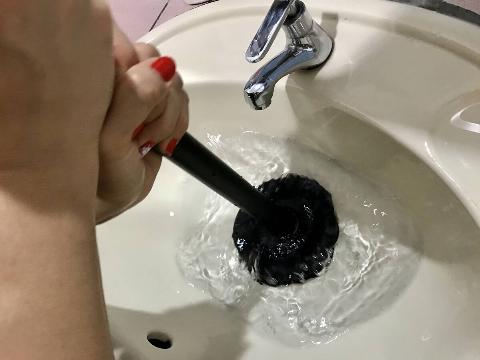 Hands using plunger to unclog sink. 