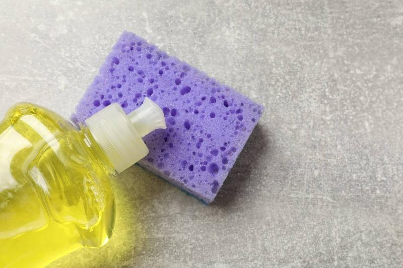 Violet sponge and dish soap on gray textured table.
