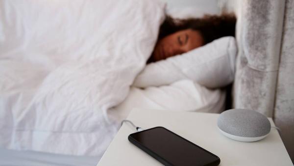 Woman asleep in bed with phone charging on. nightstand.