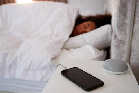 Woman asleep in bed with phone charging on. nightstand.