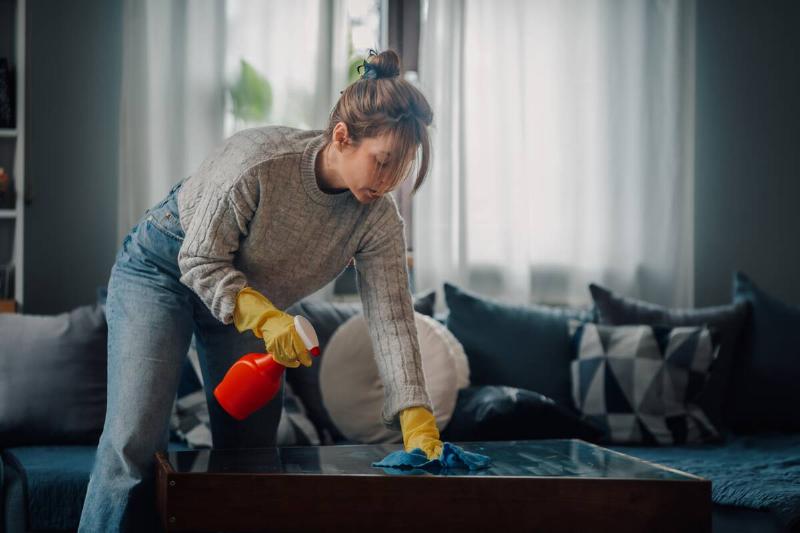 Woman cleaning coffee table in living room. 