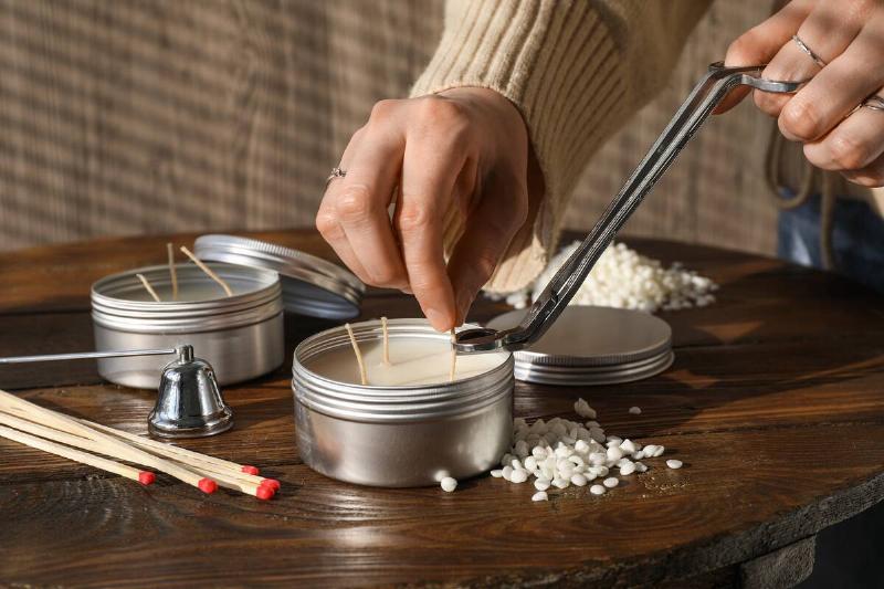 Woman cutting soy candle wick with trimmer at wooden table.