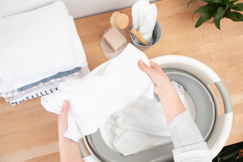 Woman putting washcloth in laundry machine.