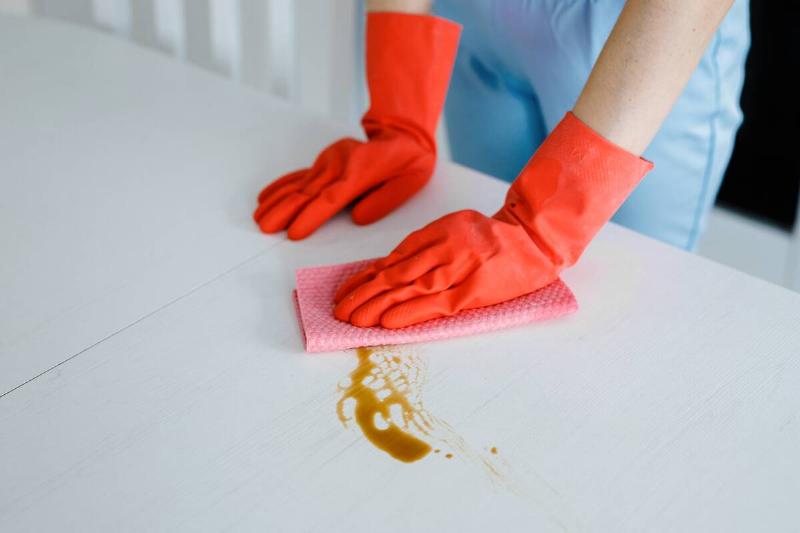 Hands wearing rubber gloves and cleaning up a spill on a white table. 