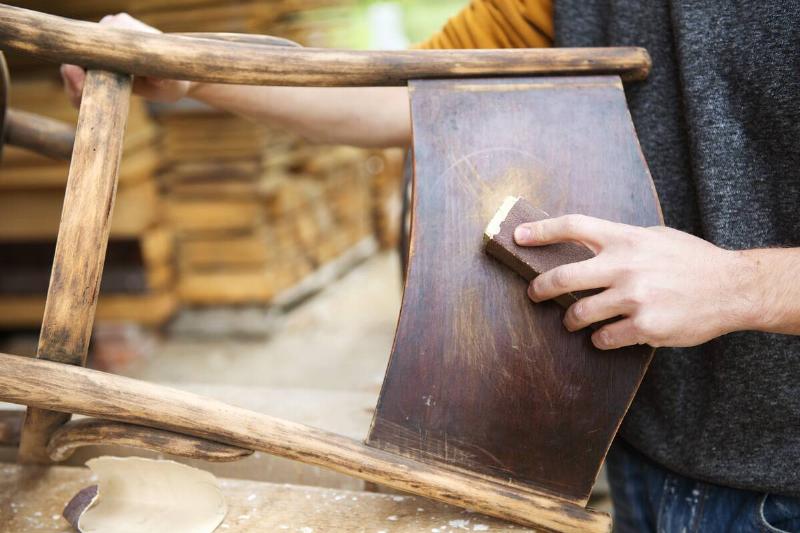 Person doing restoration work on the back of a wooden chair. 