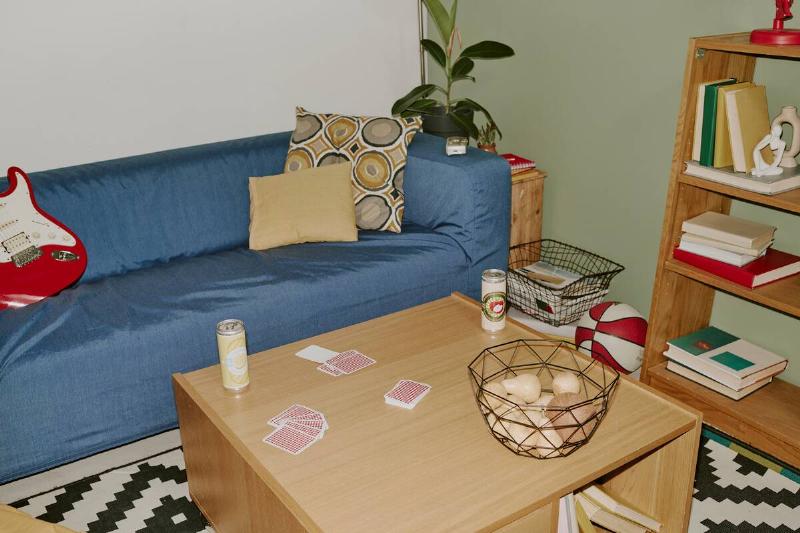 High angle shot of deep blue sofa and wooden table with lemonade cans, playing cards and metal fruit bowl.