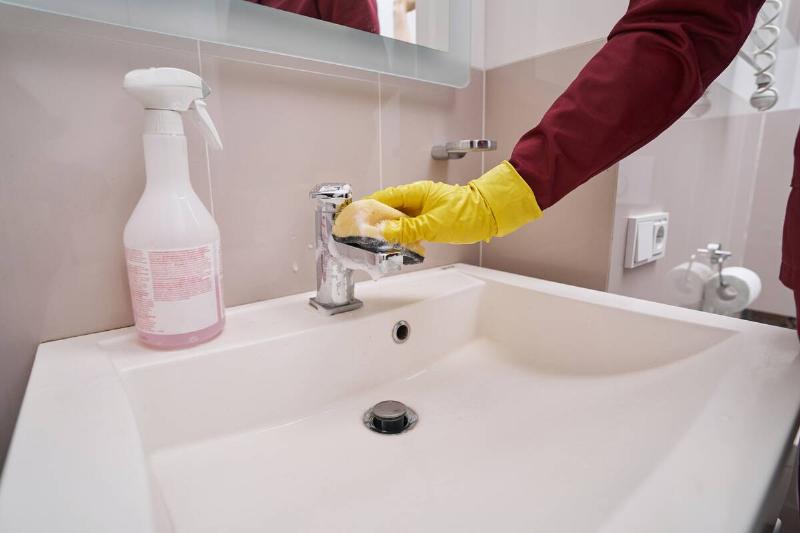 Hands in yellow rubber gloves wiping bathroom sink. 