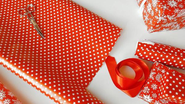 Wrapping presents in a red paper on white table close up.