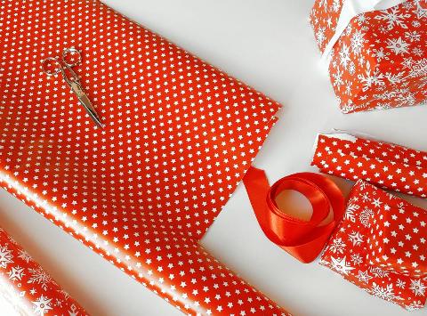 Wrapping presents in a red paper on white table close up.
