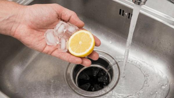 A hand putting a lemon and ice down a drain. 