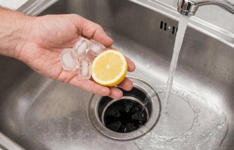 A hand putting a lemon and ice down a drain. 