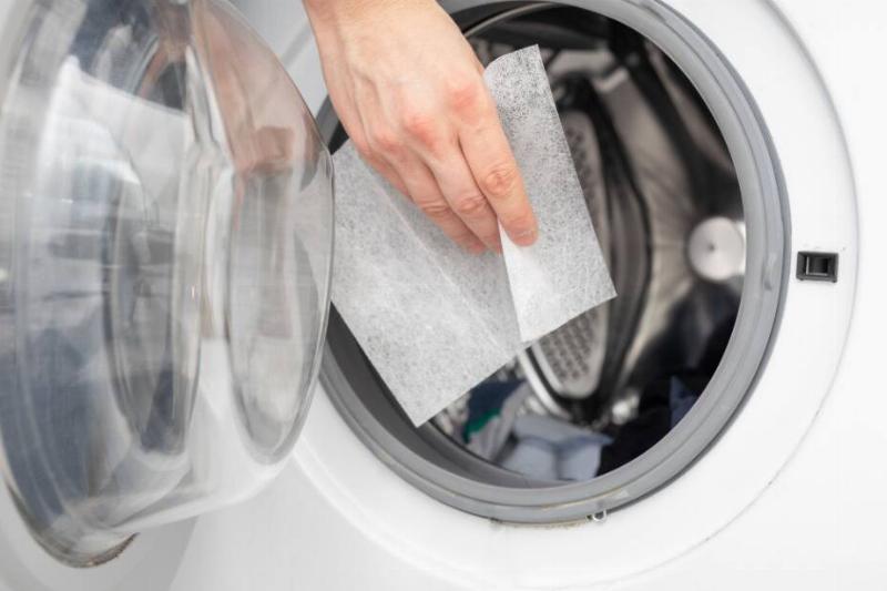 Hand putting dryer sheet in dryer.