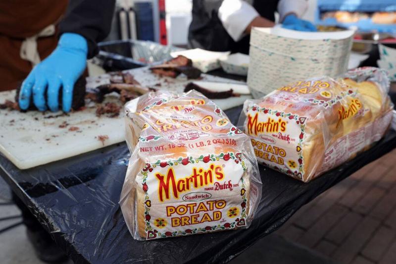 Two loaves of Martin's potato bread on a table. Two workers are cutting bread in the background