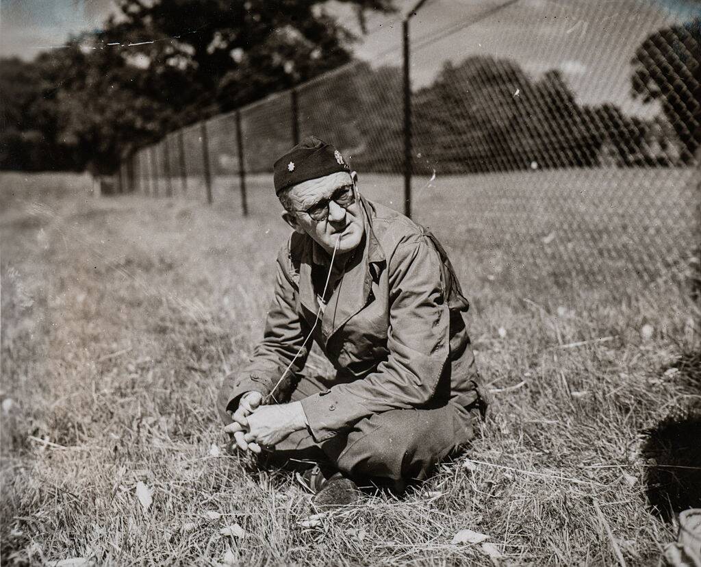 John Ford sitting in the grass, near a chain link fence