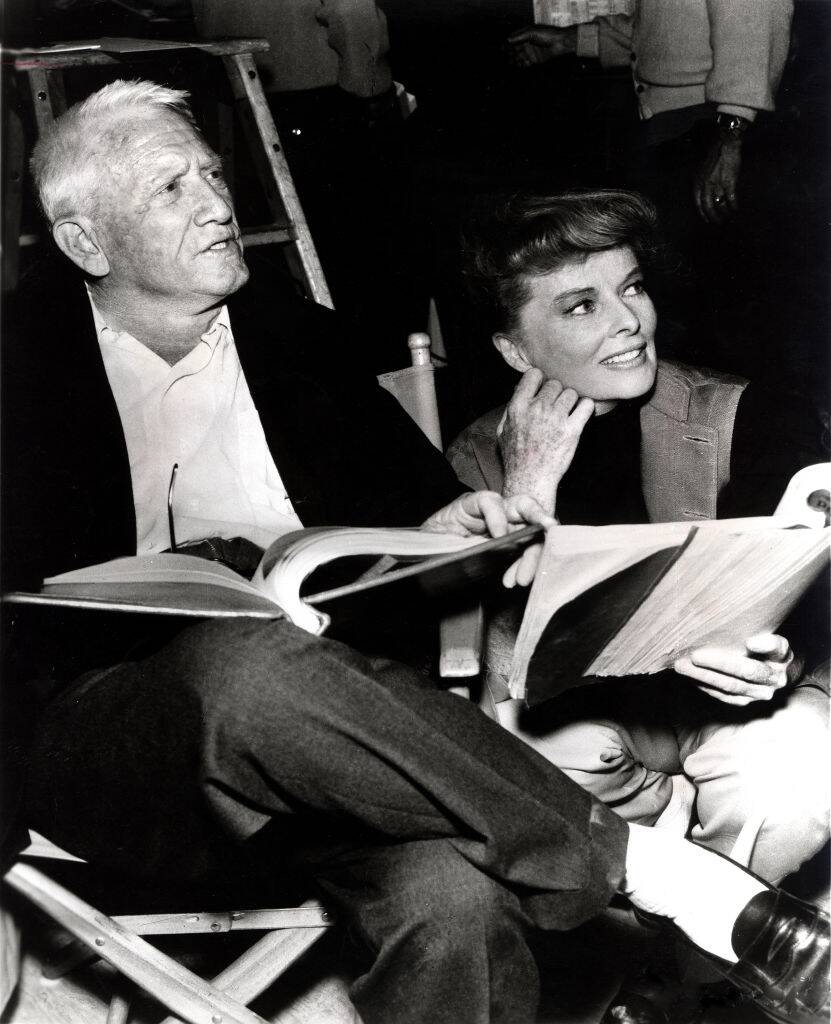 Spencer Tracy sitting in a seat, with Katharine Hepburn crouching beside him
