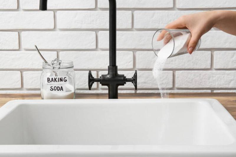 Hand pouring baking soda down sink. 