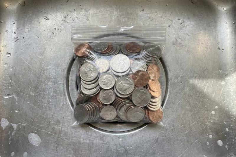 A plastic bag of coins blocking a drain.