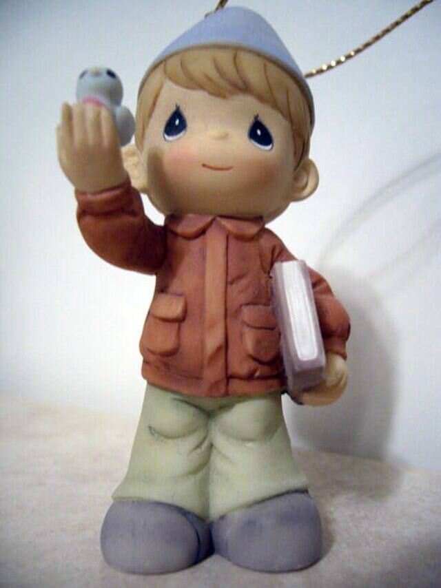 Precious Moments sculpture of a male child holding up a blue bird in one hand and a book under his other arm