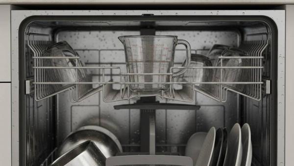 A cup of vinegar on the top rack of a dishwasher.
