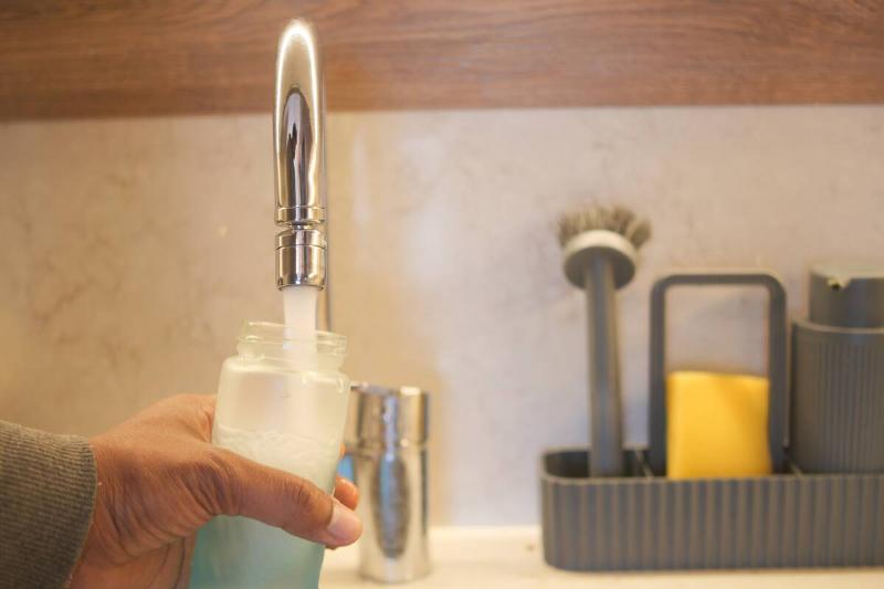 Hands filling bottle up the rest of the way with water. 