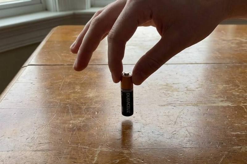 Hand holding a battery above a table.