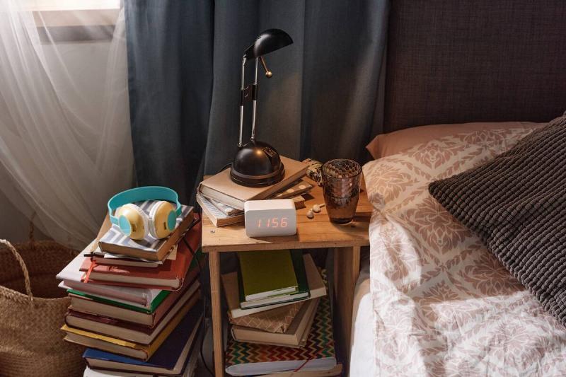 A messy nightstand that is piled high with books. 