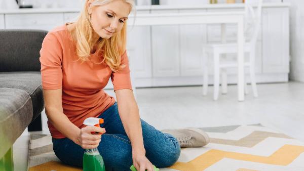 Woman cleaning carpet with vinegar spray and rag. 