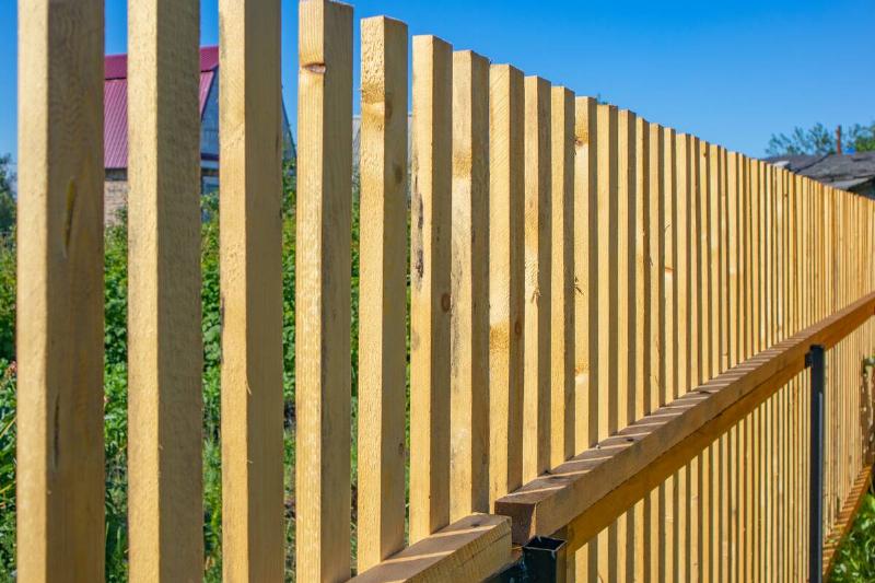 Close-up of a new wooden picket fence between two properties.