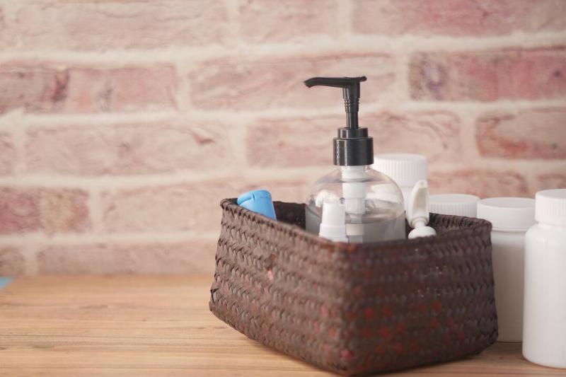 крупный план многих дезинфицирующих средств для рук в коробке на столе-2026-01-07-01-23-43-utc Корзина на деревянном прилавке с различными принадлежностями для ванной.