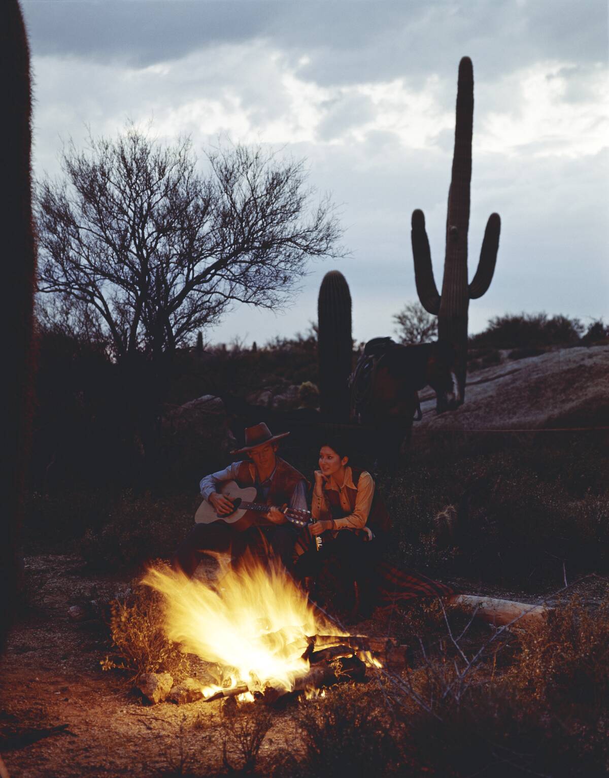 Cowboy and girl sitting beside camp fire