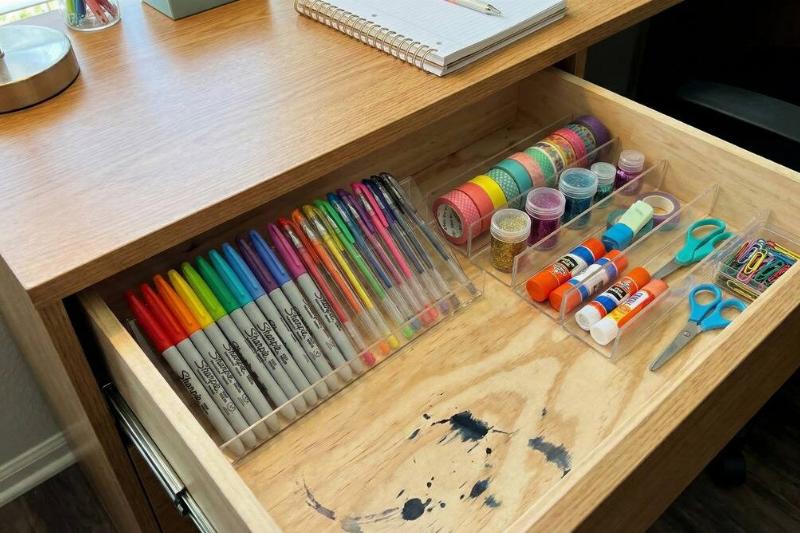 A desk drawer organized using clear picture frames. 