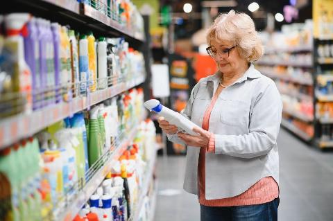 Woman reading ingredient list on cleaning products at store. 