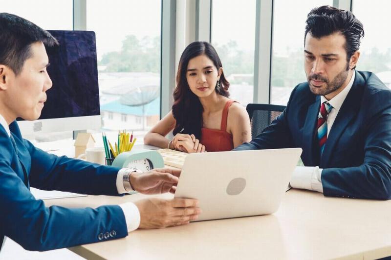 Man and a woman sitting a desk with a financial advisor, who is pointing to an open laptop screen