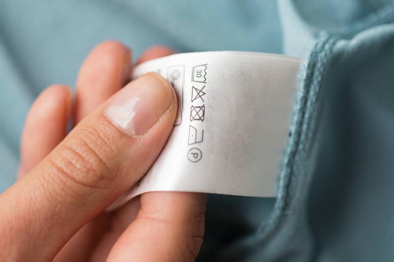 Hand holding a care label on the inside of a sheet. 