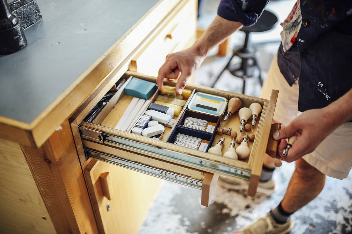 Hand reaching into drawer of art supplies. 