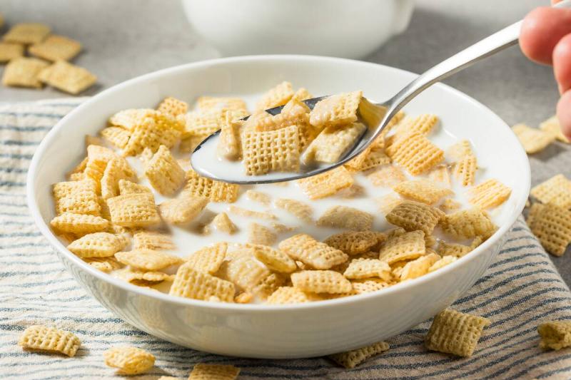 Cereal and milk in a bowl. Someone off-screen is scooping some out with a metal spoon