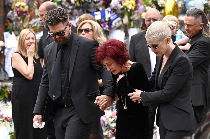 Mourners standing behind Jack, Sharon and Kelly Osbourne, all dressed in black