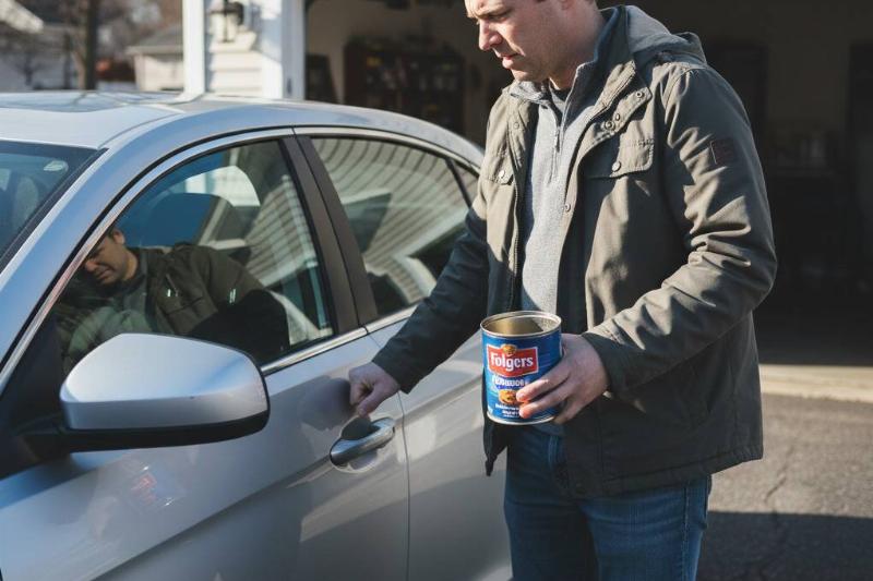 A man trying to open his car door with his keys in a coffee can.