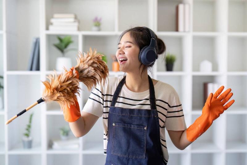 Woman singing into feather duster like microphone while cleaning. 