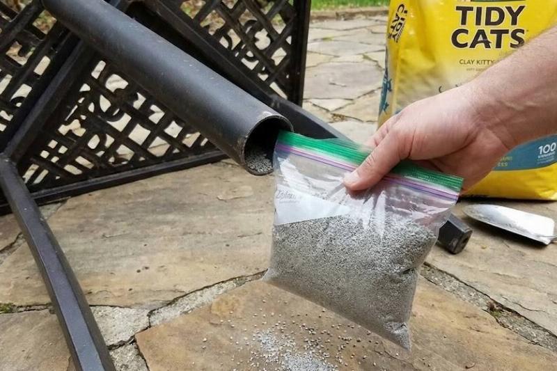 A hand putting a sealed bag of kitty litter into the leg of a patio table. 