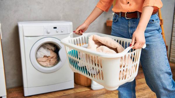 Woman holding laundry basket in front of dryer. 