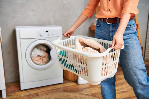 Woman holding laundry basket in front of dryer. 