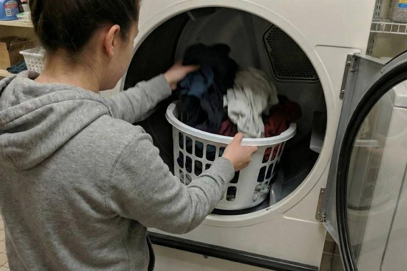 A woman putting laundry in the laundry basket inside of a dryer.