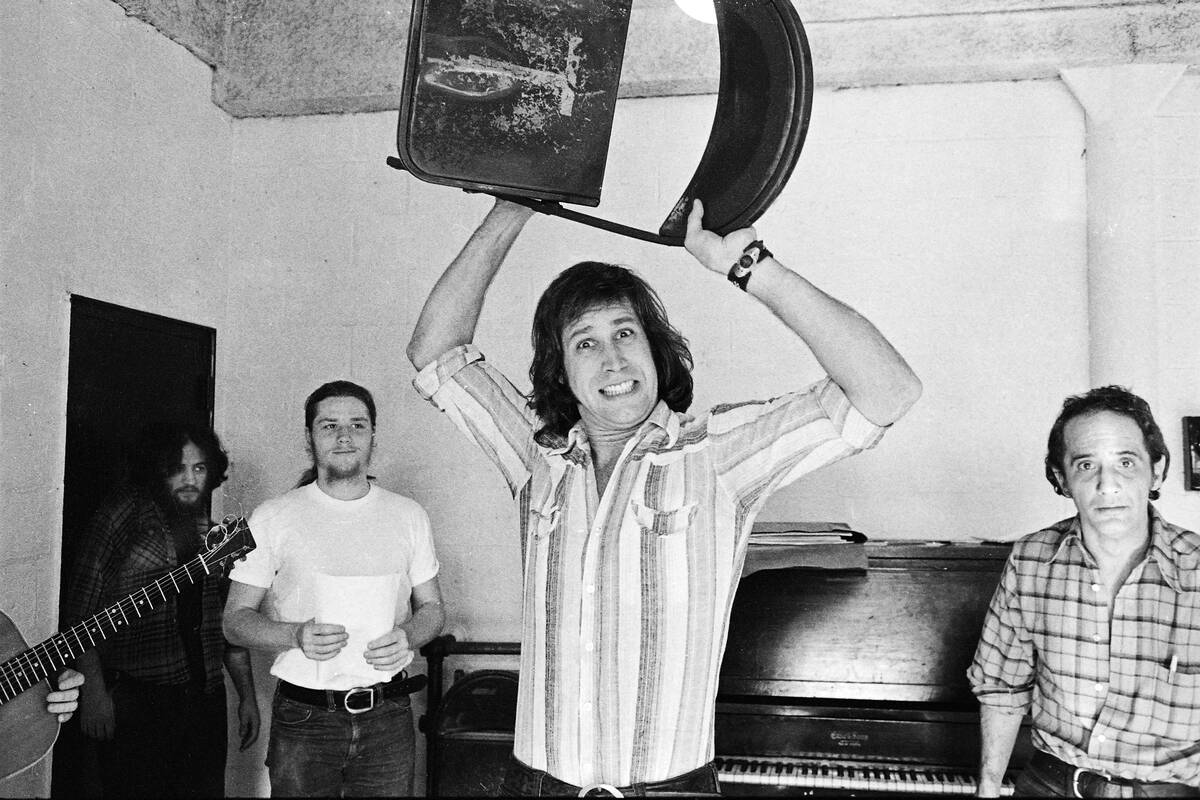 Chevy Chase standing with a chair held above his head. Men stand around him